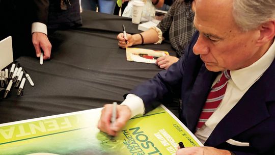 Gov. Greg Abbott writes on a poster bearing Grace Samuelson’s image June 14 after signing into law four fentanyl-related bills. The 29-year-old woman died Oct. 3, 2021, from fentanyl poisoning. Courtesy photo