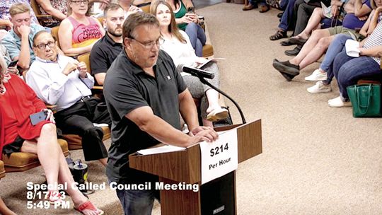 Gary Gola, a citizen speaker who was against the ordinance, holds a sign that says “$214 per hour.” Screenshot from Taylor City Council meeting