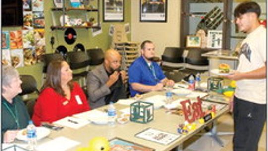 Culinary student Nick Walker presents his burger creation to the judges at Taylor High School’s Burger Challenge. From left are school board members Anita Volek and Cheryl Carter, THS principal Matt Wamble and assistant principal Sean Schobinger. Photo by Tim Crow