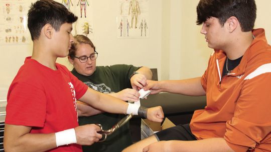 Taylor High School head athletic trainer and sports medicine instructor Taylor Huffman (center) demonstrates how to tape a wrist with students Eli Laurence (right) and Joel Lopez. The Sports Medicine CTE program has a new classroom this year with plenty of room for anatomical models, suppl...