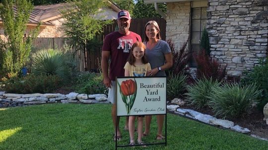 Lance and Autumn Pavlicek stand with their child in front of their winning yard for the Taylor Garden Club’s Beautiful Yard Award. Courtesy photo