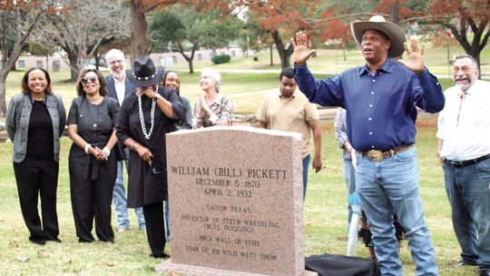 (Front row, from left) Ursurla Williams, Michelle Anderson, Dannie Royal, (back row from left) Mayor Brandt Rydell, Nekoya Anderson, Nancy Hill, Leroy Anderson and Mike Kaspar listen as District 1 Councilman Gerald Anderson addresses the crowd during the unveiling of the Bill Pickett cenot...