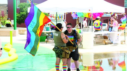 Gen Peńa of Veterans for Equality stands with a Pride flag near the splash pad area of Heritage Park. Photo by Hunter Dworaczyk