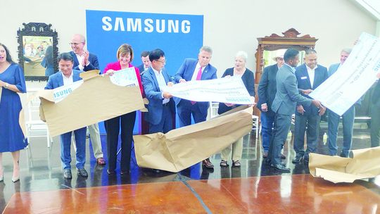 Members of local organizations unwrap giant $250,000 checks at a Samsung announcement event. Photo by Jason Hennington