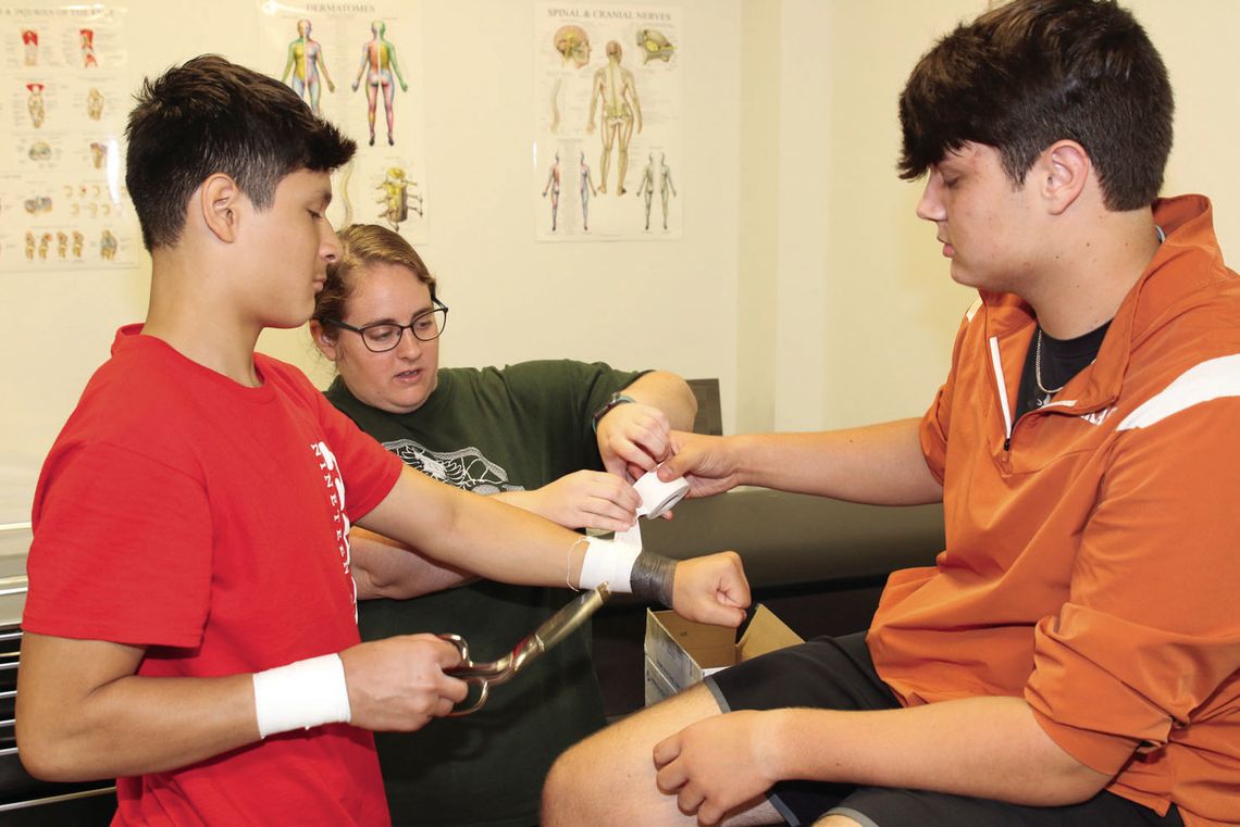 Taylor High School head athletic trainer and sports medicine instructor Taylor Huffman (center) demonstrates how to tape a wrist with students Eli Laurence (right) and Joel Lopez. The Sports Medicine CTE program has a new classroom this year with plenty of room for anatomical models, suppl...