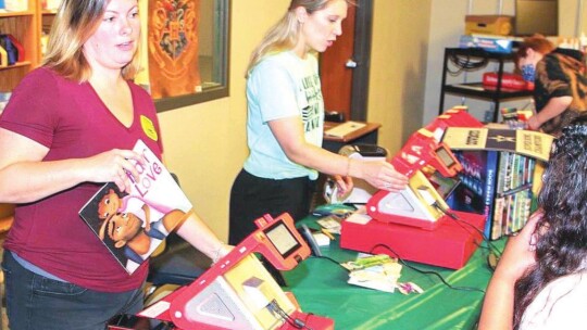 Taylor-Aides volunteer Misty Murtha (left) helps Main Street Intermediate School librarian Vanessa Collier with the school’s book fair.