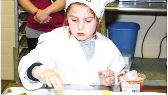 Harper Doss adds the finishing touches to her dish, “Dragons Love Tacos – Taco Bake” before it goes to the judges for tasting.