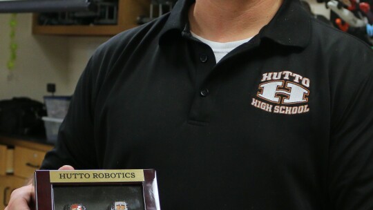 Andrew Haub, coach of the Hutto HS robotics team known as RoboCo X, shows off the four state championship rings his robotics team has won for Hutto.