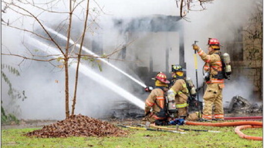 While battling the cold and rain, firefighters spray water on a burning house Monday afternoon.