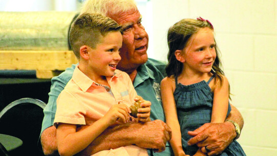 Sam Dowdy Sr. sits with grandkids as his son gives his remarks.